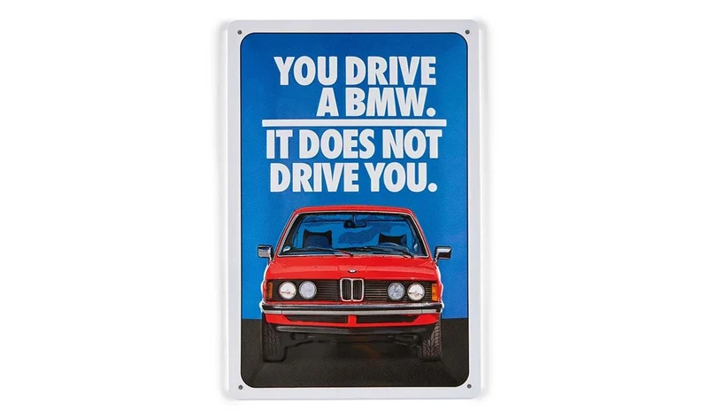Cartel de hojalata BMW Lifestyle Primavera/Verano 2025, azul/rojo/blanco, dimensiones 280x200 mm, con texto "You drive a BMW. It does not drive you." y modelo E21. Válido para BMW. Original BMW.